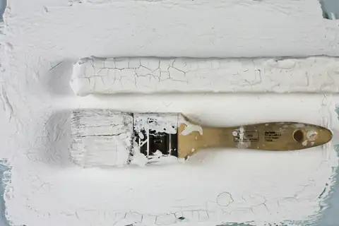Paintbrush with white paint resting on a freshly painted white surface