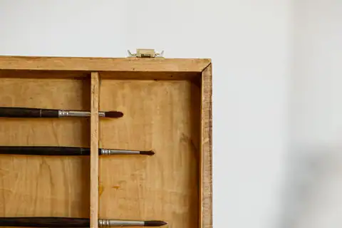Paintbrushes laid across the shelves of a wooden cabinet