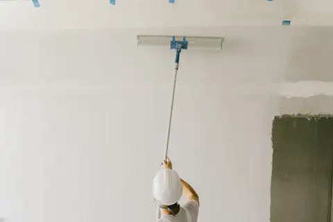 Painter seen from behind, rolling a wall with an extension pole, blue tape along the ceiling