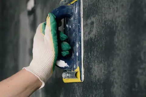 Gloved hand smoothing patching compound on a dark wall with a plastering tool